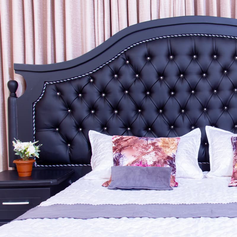 Detail of a black tufted headboard with floral scatter cushions and champagne curtains.