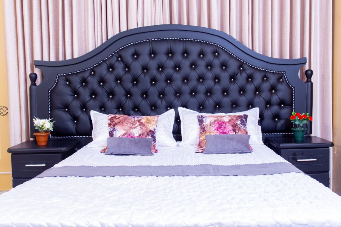 Neatly made double bed with a black tufted headboard, crisp white bedding and rose posies either side.