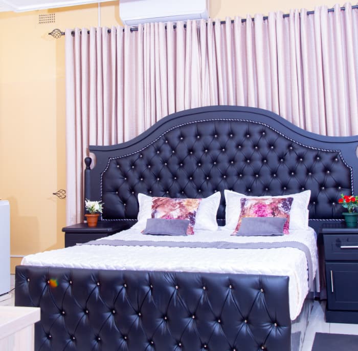 Elegant room with a black button-tufted bed, soft cream curtains and fresh roses on the nightstands.