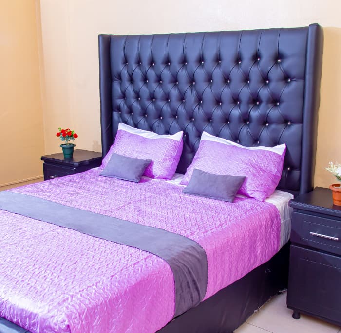 Bright room dressed in magenta and grey linen against a tall tufted headboard.